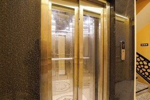 Un ascensor con puerta de vidrio, un panel de control con pantalla digital y suelo de mármol.