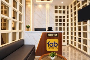 Un área de recepción con una pared de mármol, un mostrador de recepción que dice 'fab hotels', un sofá negro y una planta en maceta.
