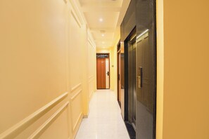 A hotel corridor with a marble floor, a wooden door, and a black elevator. - FabHotel Saroja Royal Stay (Varanasi)