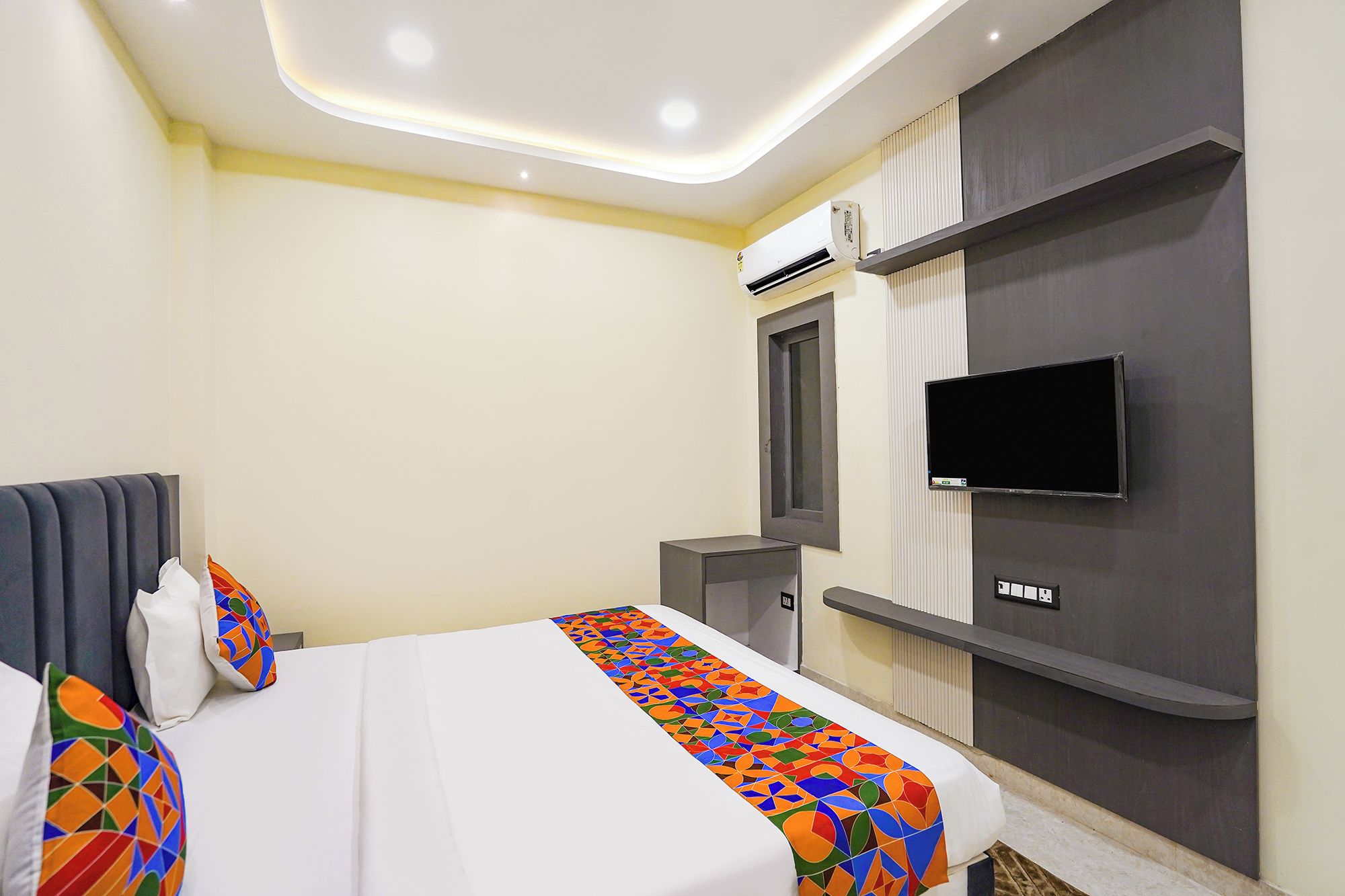A hotel room with a bed, a TV mounted on the wall, and a small desk.