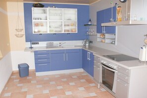 Een keuken met blauwe kastjes, een wit aanrecht, een spoelbak, een fornuis en een prullenbak.