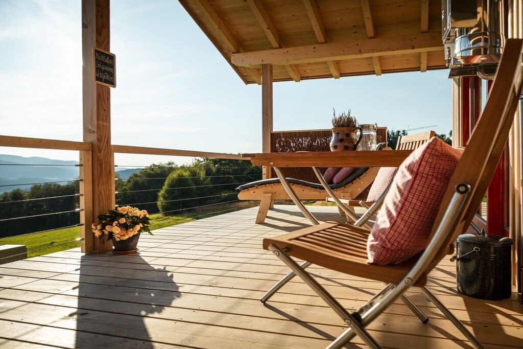 A wooden deck with a lounge chair and a table with a kettle and flowers.