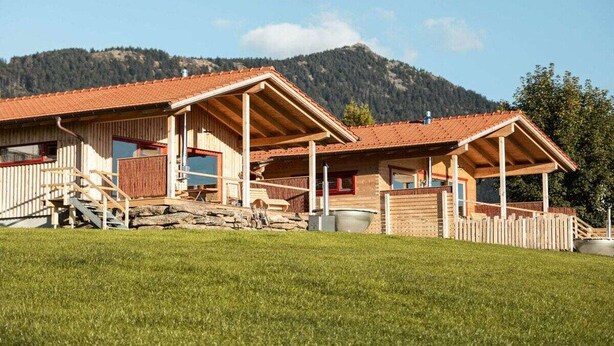 Een houten chalet met een rode dakbedekking, een stenen fundering en een houten omheining.