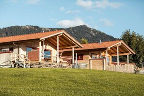 Een houten chalet met een rode dakbedekking, een stenen fundering en een houten omheining.