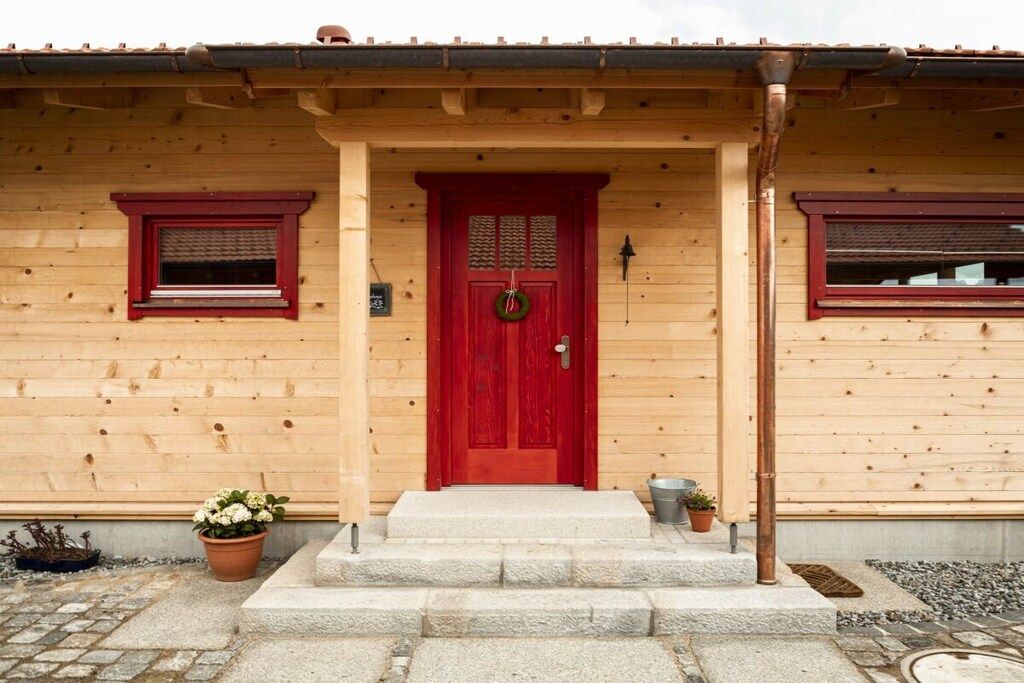 Ein Holzgebäude mit roter Tür, einer kleinen Veranda und Stufen zum Eingang.