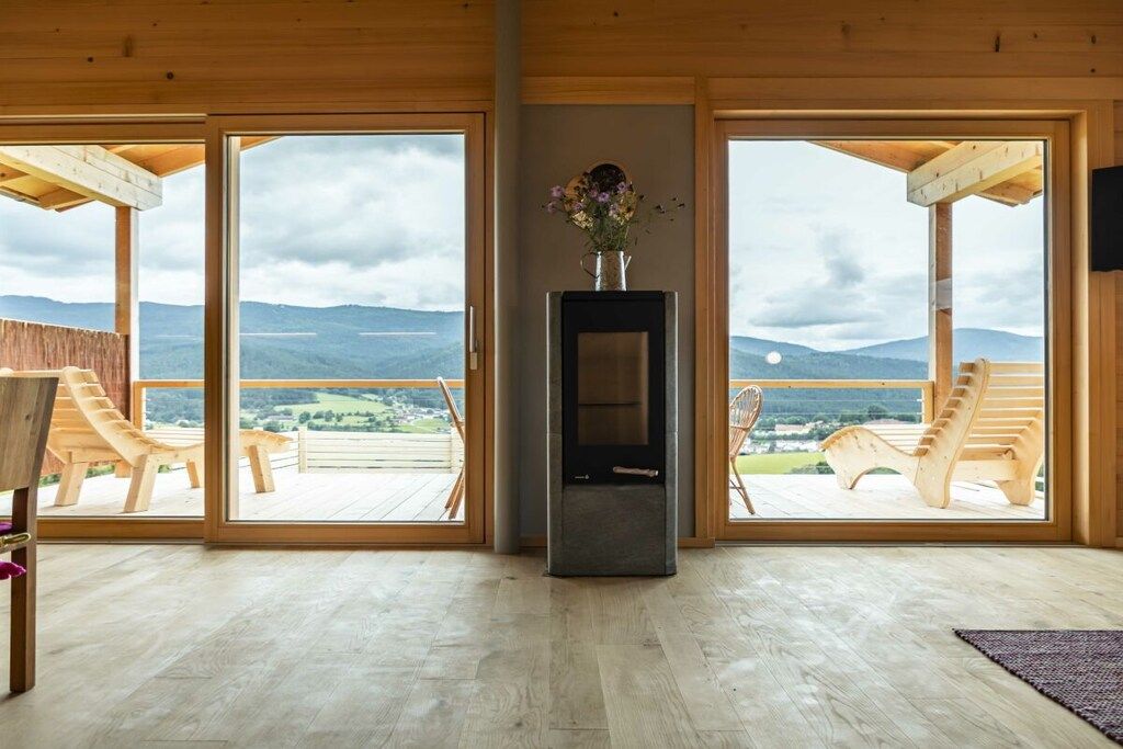 Une pièce avec une cheminée, deux fauteuils en bois et une grande fenêtre donnant sur les montagnes.