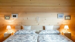 Een tweepersoonsbed met een sprei met bladmotief, twee nachtkastjes met lampen en ingekaderde certificaten aan de muur.