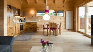Een houten interieur met een eethoek, keuken en grote ramen.