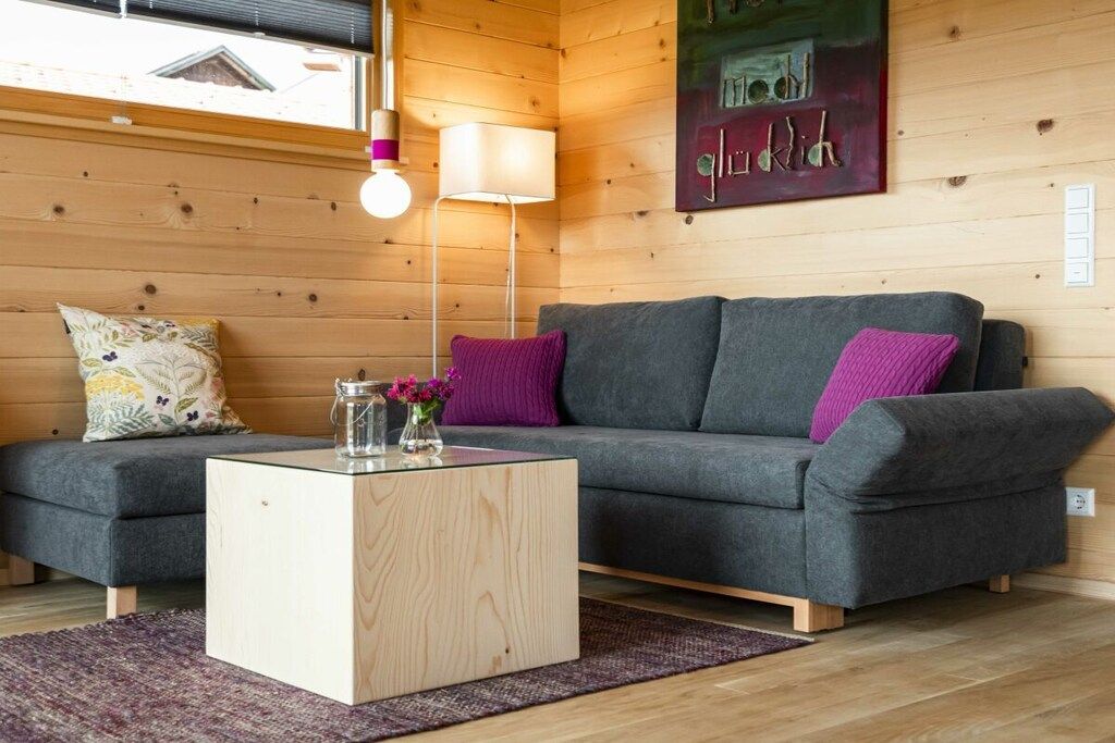 Ein gemütliches Zimmer mit einem grauen Sofa, einem Holztisch und einer Lampe.