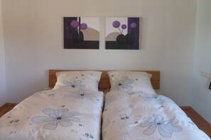 A bedroom with a double bed, two wall-mounted paintings, and a floral-patterned bedspread. - Holiday apartment in Vöhl with swimming pool (Vöhl)
