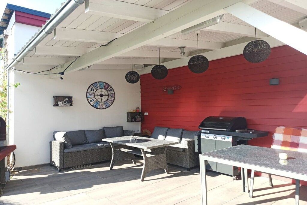 Eine Terrasse im Freien mit roter Wand, einem Grill, Korbmöbeln und einer Wanduhr.