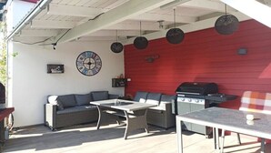 Una terrazza esterna con un muro rosso, un barbecue, mobili in vimini e un orologio a parete.