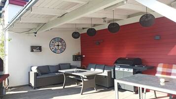 Eine Terrasse im Freien mit roter Wand, einem Grill, Korbmöbeln und einer Wanduhr.