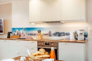 Eine Küche mit weißen Schränken, einem Herd, einer Kaffeemaschine und einem Gemälde einer verschneiten Winterlandschaft.