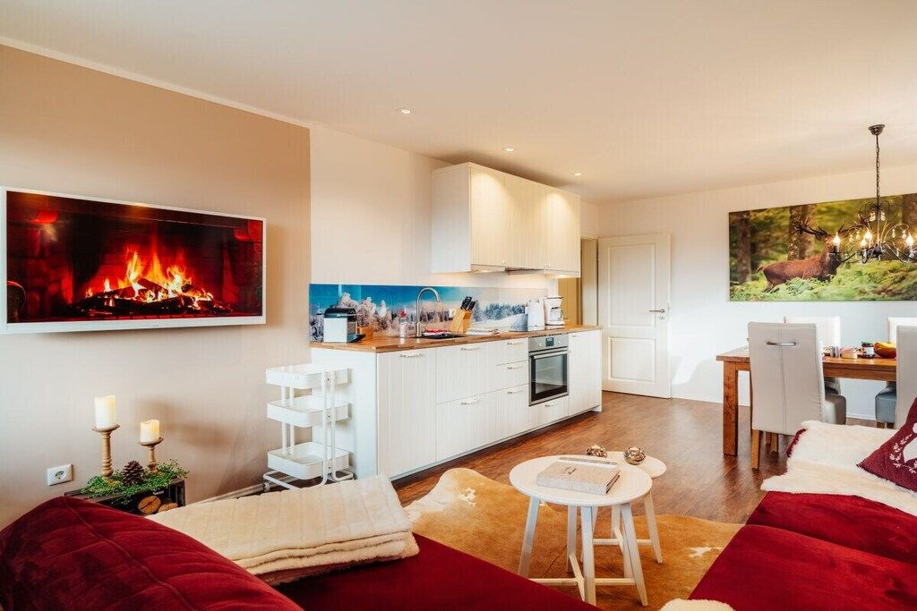 A modern living room with a fireplace, a dining area, and a kitchen with white cabinetry.
