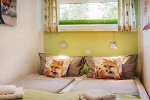 Ein Schlafzimmer mit zwei Betten, jedes mit einem Kissen mit einem Fuchs-Design, einem Fenster mit grünen Jalousien und einem wandmontierten Lichtschalter.