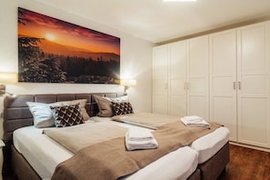 A bedroom with a large bed, a wardrobe, and a painting of a sunset. - Holiday apartment with 1 bedroom (Braunlage)