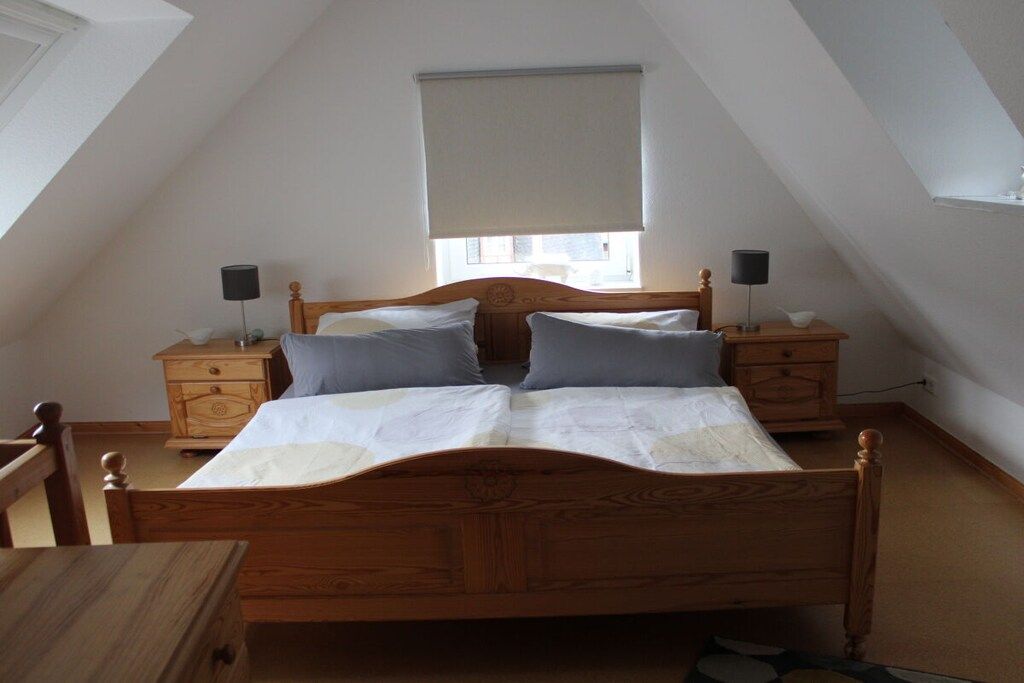 Ein Schlafzimmer mit einem hölzernen Bett, zwei Nachttischen, einem Fenster mit Jalousie und einer geneigten Decke.