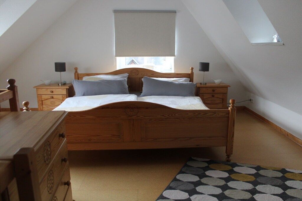 Een slaapkamer met een houten bed, twee nachtkastjes, een dressoir, een raam met een rolgordijn en een kamerbreed tapijt met een patroon.