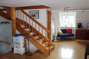A wooden staircase leading to a loft bedroom, a kitchenette with a window, and a blue sofa in a living area. - Bremmer Hof " Stubenblick" (Bremm)