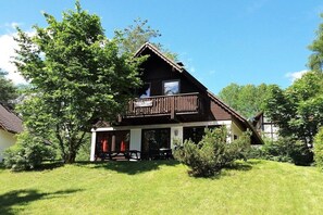 A two-story wooden house with a balcony, surrounded by greenery and trees. - Gingerbread House Gretel (Frankenau)