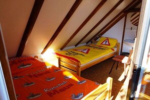 A small, single-bed room with a sloped ceiling, a wooden bed frame, and a yellow bedspread with a warning sign. - Gingerbread House Gretel (Frankenau)