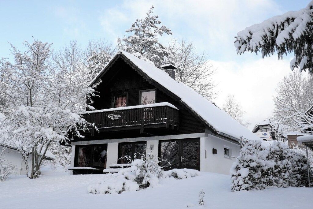 A two-story lodge with a balcony, surrounded by snow-covered trees.