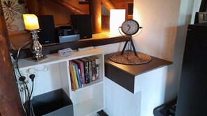 A room with a wooden ceiling, a white shelf with books, a clock on a stand, and a lit candle. - Gingerbread House Gretel (Frankenau)