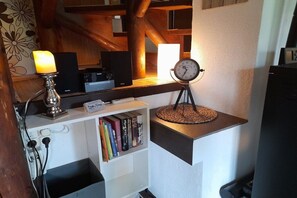Ein Zimmer mit Holzboden, einem weißen Regal mit Büchern, einer auf einem Podest stehenden Uhr und einer brennenden Kerze.