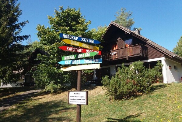 A signpost with distances to various cities and a contact information sign below it. - Gingerbread House Gretel (Frankenau)