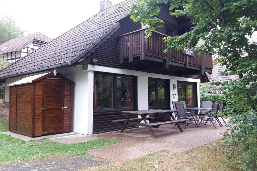 Een gebouw met een houten gevel, een balkon en een picknicktafel met stoelen.
