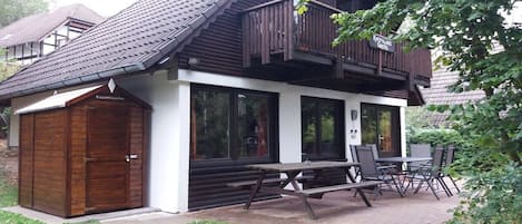 Un edificio con fachada de madera, un balcón y una mesa de picnic con sillas.