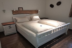 Ein Schlafzimmer mit einem weißen Bett, zwei Nachttischen, einem Holzkopfstück und einem Beistelltisch.