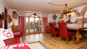 A cozy room with a wooden dining table, red chairs, a sofa with red cushions, and a fireplace with a decorative arch. - Holiday apartment with 2 bedrooms (Tittmoning\/Törring)