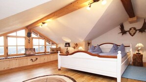 A bedroom with a sloped ceiling, wooden beams, a bed with a headboard, a window with a view, and wall-mounted decor. - Holiday apartment with 2 bedrooms (Tittmoning\/Törring)