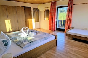 A bedroom with a large bed, a smaller bed, wooden flooring, a balcony with red curtains, and a hanging light fixture. - Holiday apartment with 1 bedroom (Lohberg)