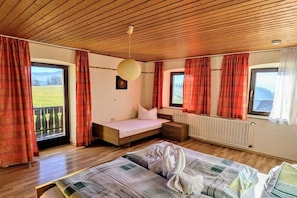 A bedroom with a wooden ceiling, a bed with a striped blanket, a bedside table, a window with curtains, and a view of the outdoors. - Holiday apartment with 1 bedroom (Lohberg)