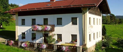 A two-story building with a red-tiled roof, white walls, and a balcony with flower boxes.