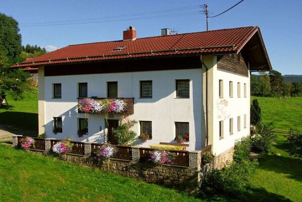 A two-story building with a red-tiled roof, white walls, and a balcony with flower boxes. - Holiday apartment with 1 bedroom (Lohberg)
