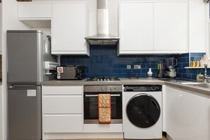 A compact kitchen with a refrigerator, oven, washing machine, and a gas stove. - New! Modern 2BR Flat | Forest Gate (Greater London)