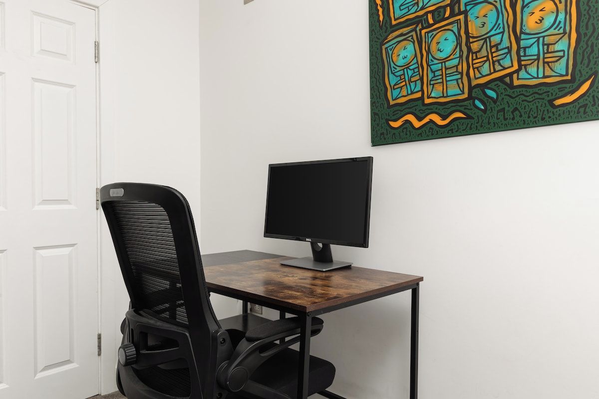 Uma área de trabalho com escrivaninha, monitor de computador e cadeira.