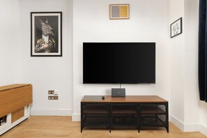 A living room with a large flat-screen TV mounted on the wall, a wooden entertainment unit below, and a framed artwork on the wall. - New! Modern 2BR Flat | Forest Gate (Greater London)