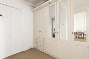 Ein Zimmer mit einem weißen Kleiderschrank, einem Spiegel und einer Tür zu einem weiteren Raum.