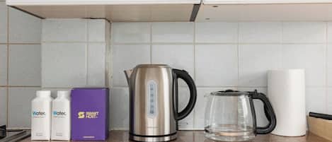 A kitchen counter with a stainless steel kettle, two water bottles, a purple box, and a glass pitcher.