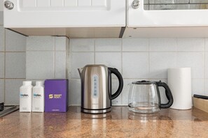 A kitchen counter with a stainless steel kettle, two water bottles, a purple box, and a glass pitcher. - New! Inviting 1BR Flat in Woolwich (Greater London)