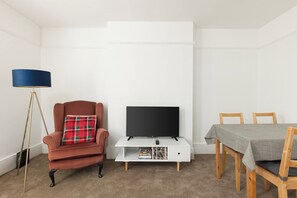 A room with a sofa, a television on a stand, a dining table with chairs, and a floor lamp. - New! Inviting 1BR Flat in Woolwich (Greater London)
