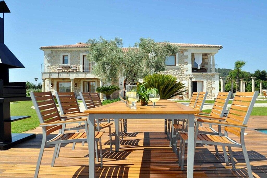 Une terrasse en bois avec une table et des chaises, un bâtiment en pierre en arrière-plan et un ciel dégagé.