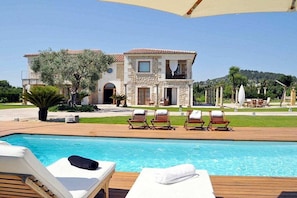 A poolside area with lounge chairs and a clear view of a two-story building with a stone facade and a tiled roof. - Ses Rentedores [2257] (Selva)