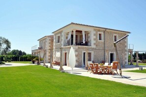 A two-story stone building with a balcony, outdoor seating, and a well-maintained lawn. - Ses Rentedores [2257] (Selva)