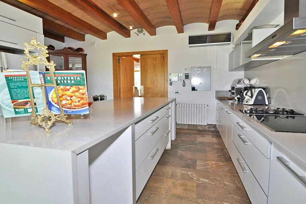Une cuisine moderne avec des meubles blancs, un îlot central, une cuisinière et un plafond en bois.